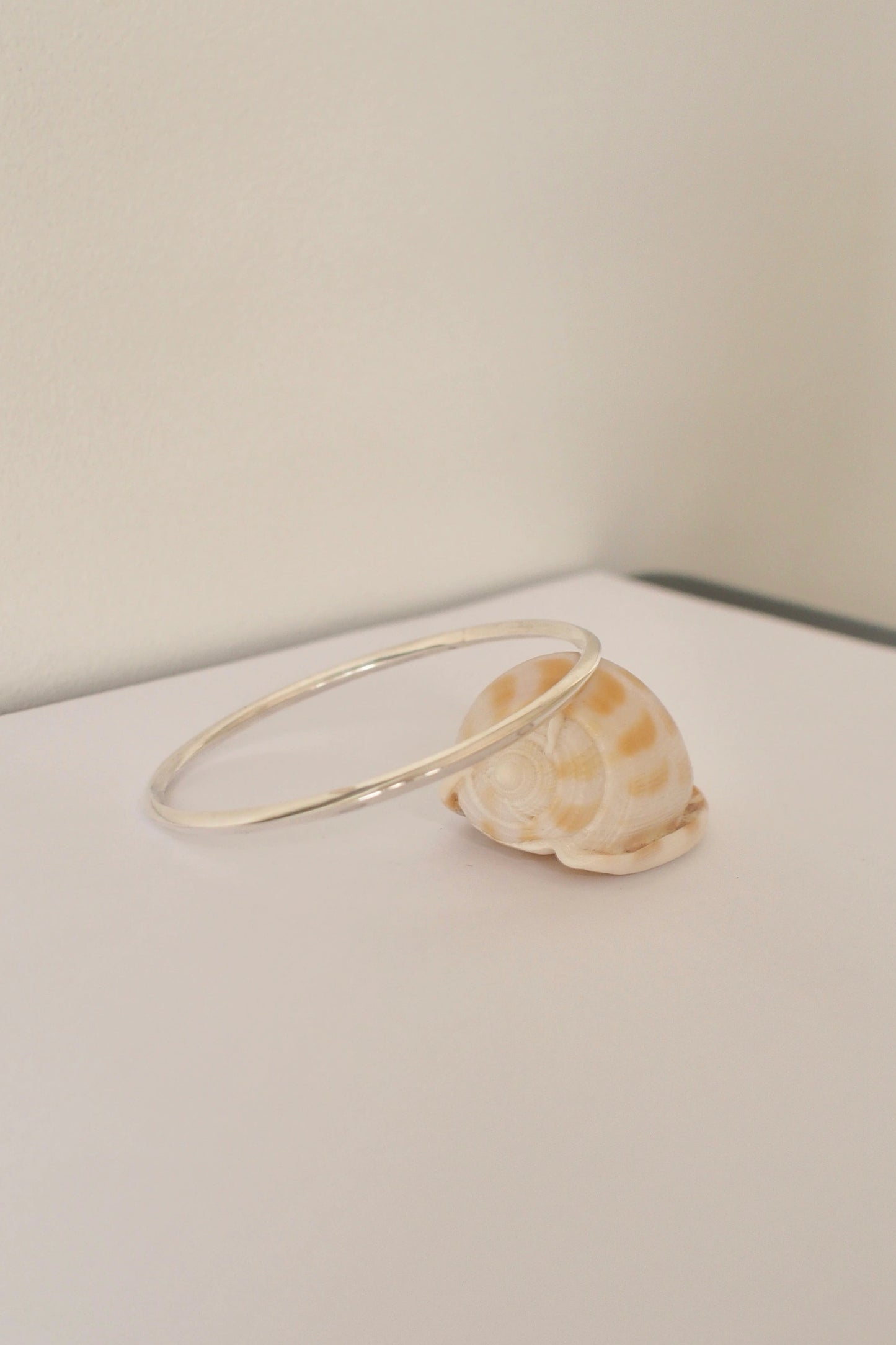 silver bangle on a white surface with a neutral background