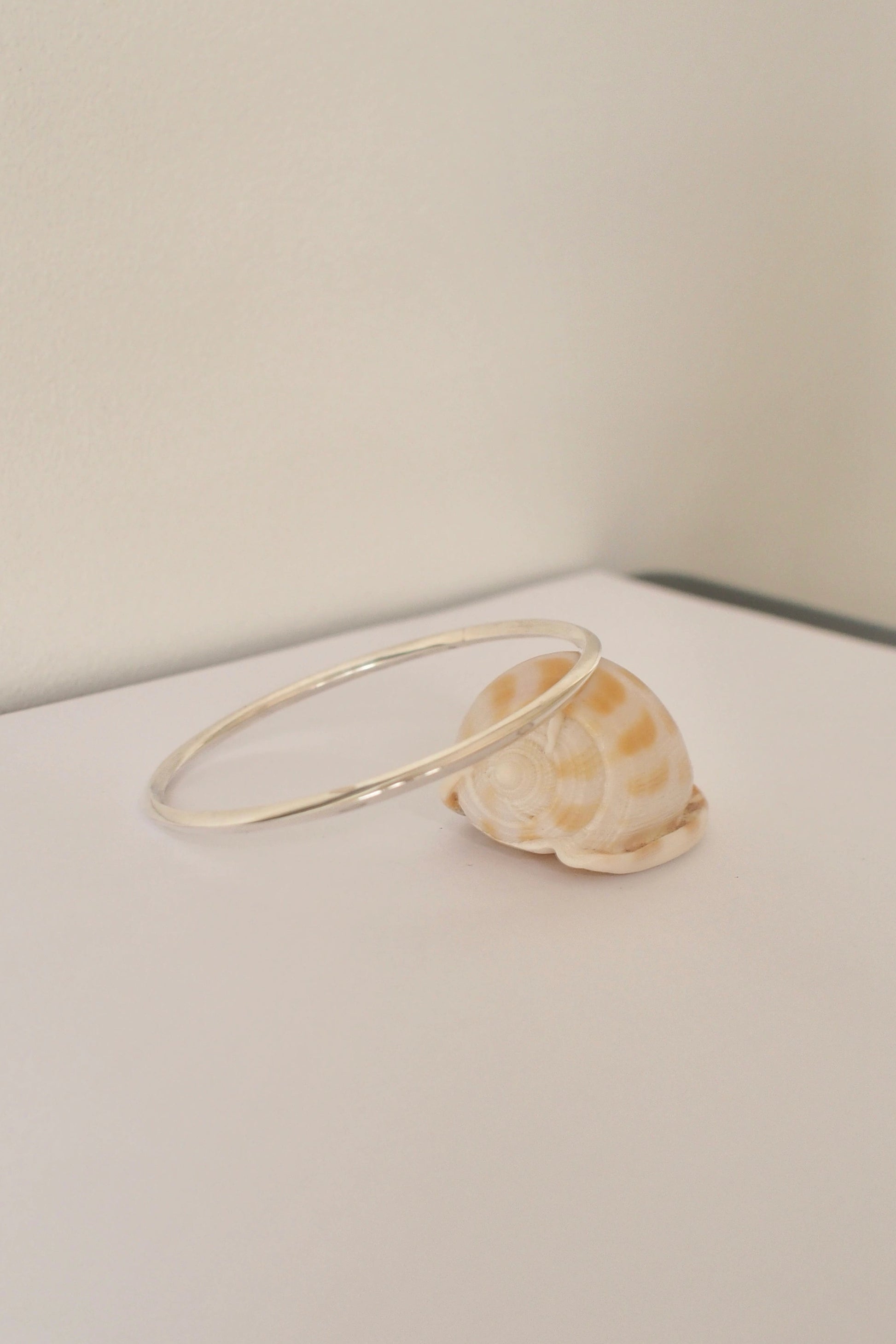 silver bangle on a white surface with a neutral background