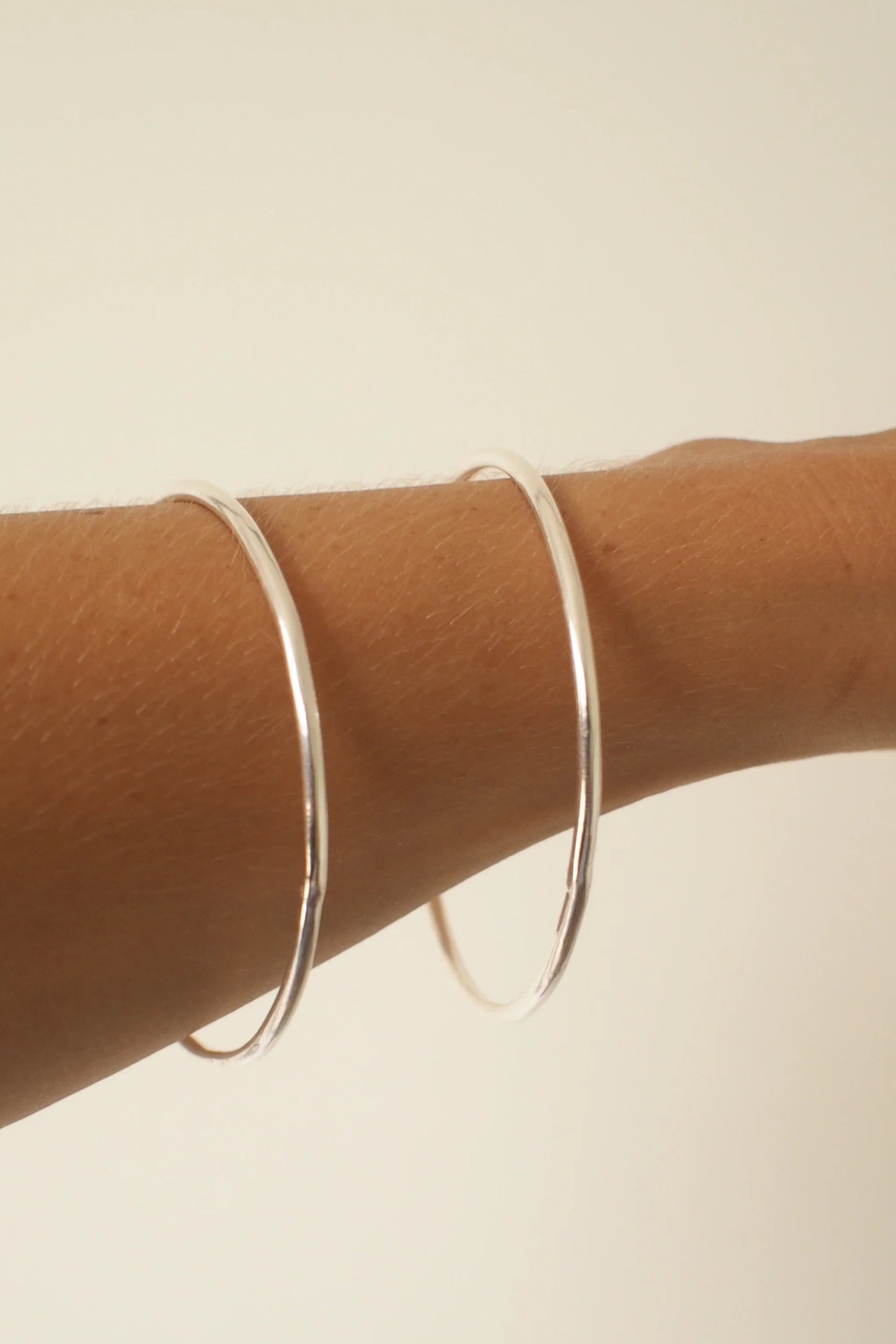 Silver bangles on a person's wrist against a beige background