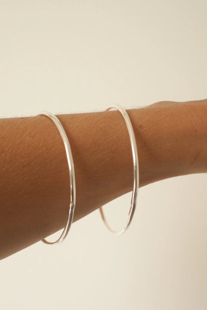 Silver bangles on a person's wrist against a beige background