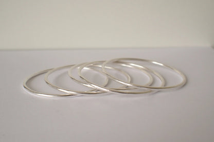 Set of silver bangles on a light gray surface