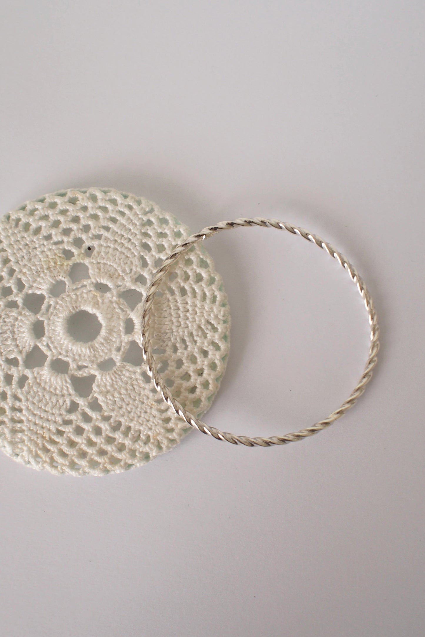 Doily and twisted silver bangle on a light gray surface