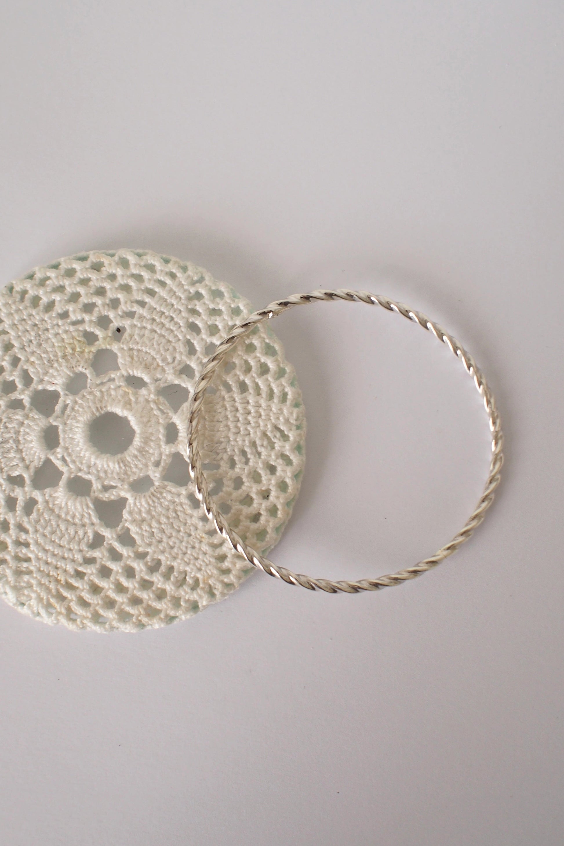 Doily and twisted silver bangle on a light gray surface