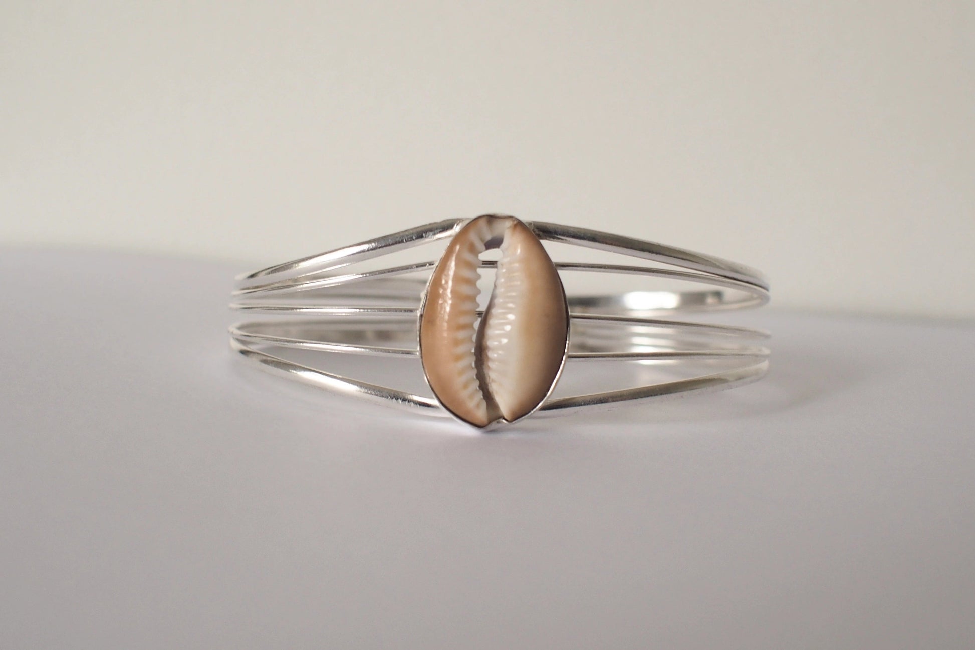 Silver bracelet with a cowrie shell on a light gray background