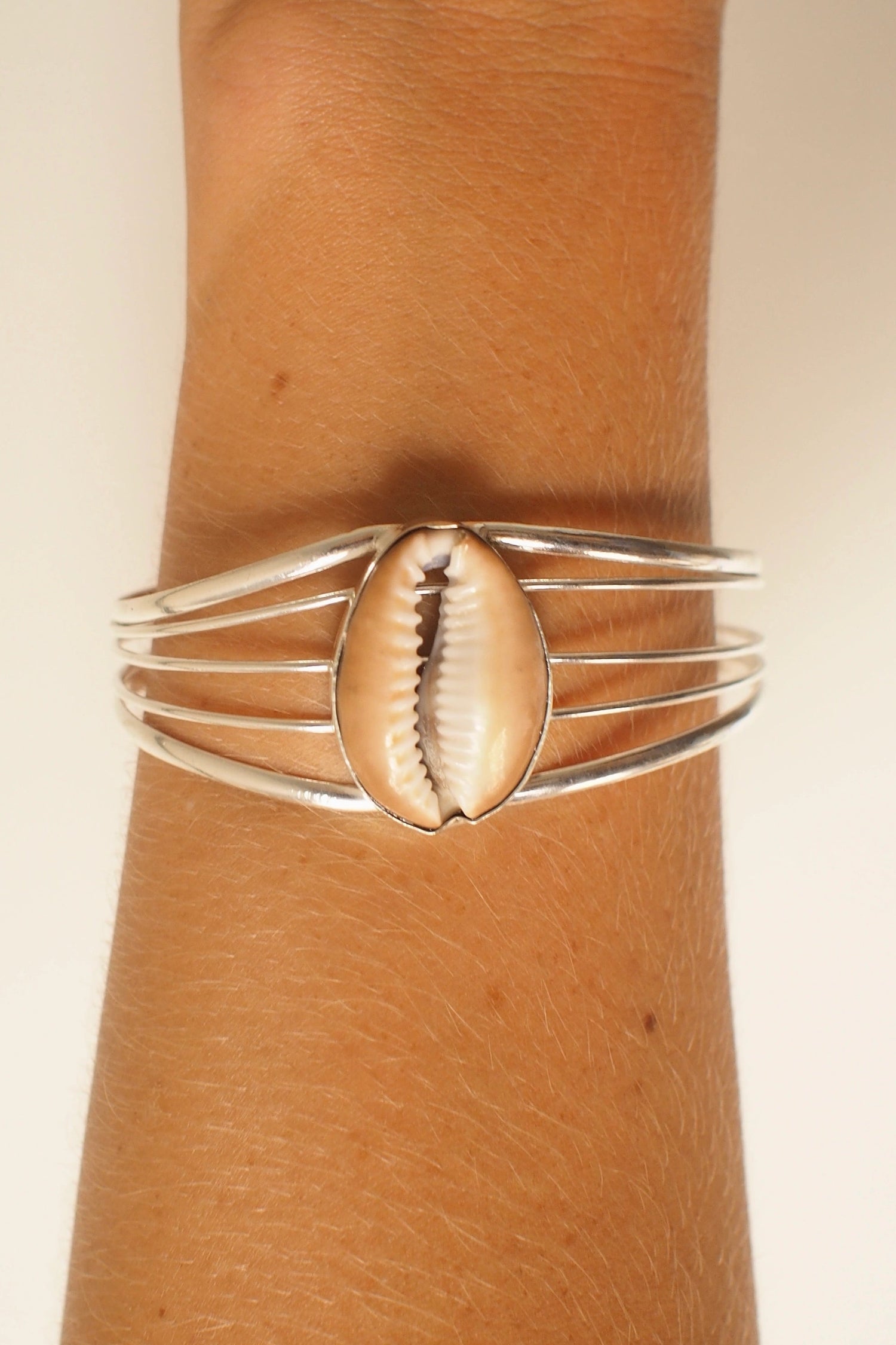 Silver bangle bracelet with a shell design on a wrist against a beige background